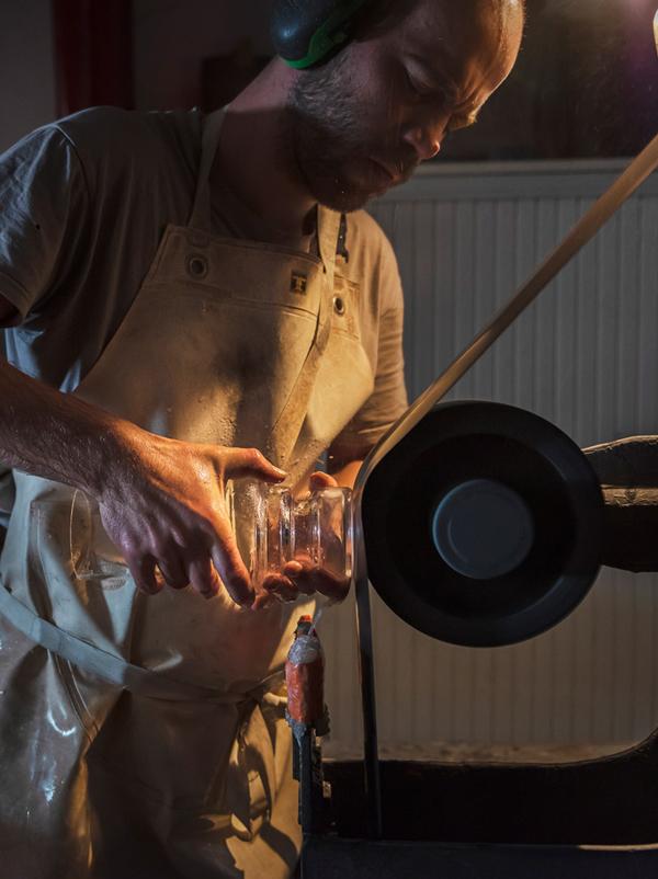 Simon muller polit un objet en verre dans l'obscurité de son atelier Arcam glass à Vertou. Il travaille pour la création contemporaine, sur des projets de designers, artistes plasticiens, architectes, décorateurs ou privés.