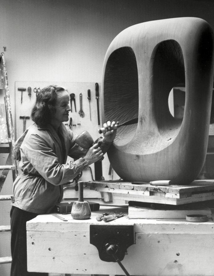 Barbara Hepworth sculpte dans un tronc d'arbre dans son atelier.