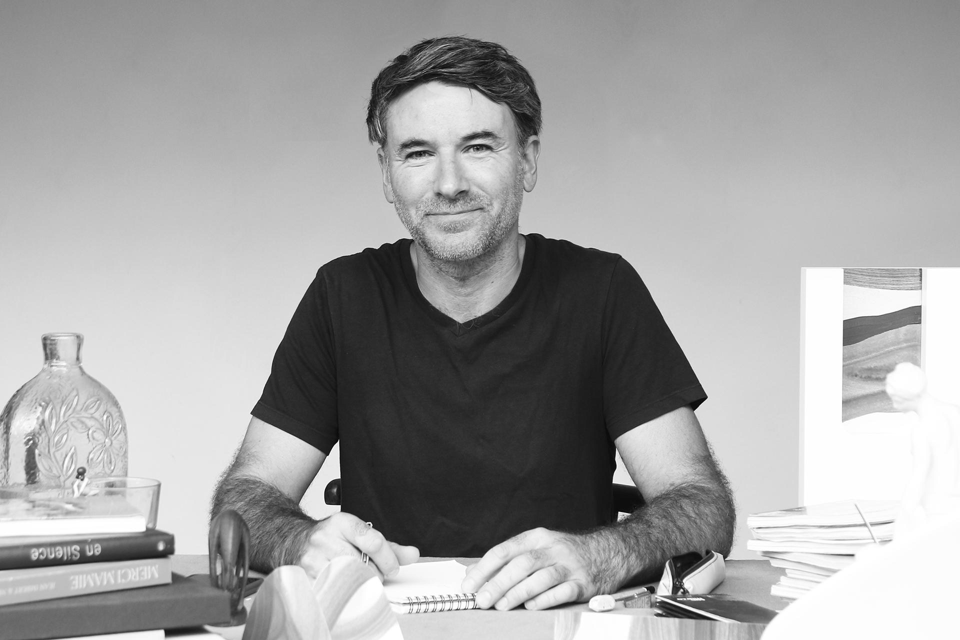 Portrait en photo de Jerome Barrier designer d'intérieur. Mobilier et intérieurs sur-mesure en Loire atlantique. en noir et blanc sur sa table de travail avec un carnet à dessin.