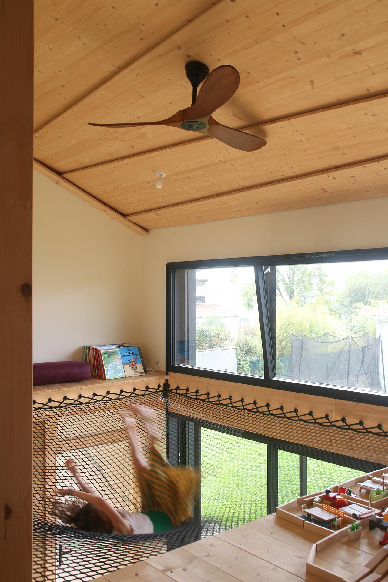 Un enfant saute dans le filet d'habitation au dessus d'un plafond décor découpé dans dans des panneaus 3 plis épicéa.