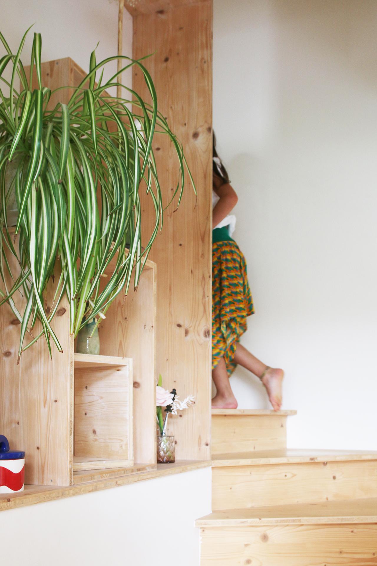 Un enfant monte dans l'escalier. Les marches contournent une haute bibliothèque avec des rangements astucieux et flexibles. Design Jérôme Barrier création sur mesure.